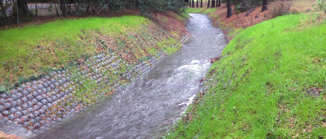 Grassed channel banks beside a rock-lined waterway