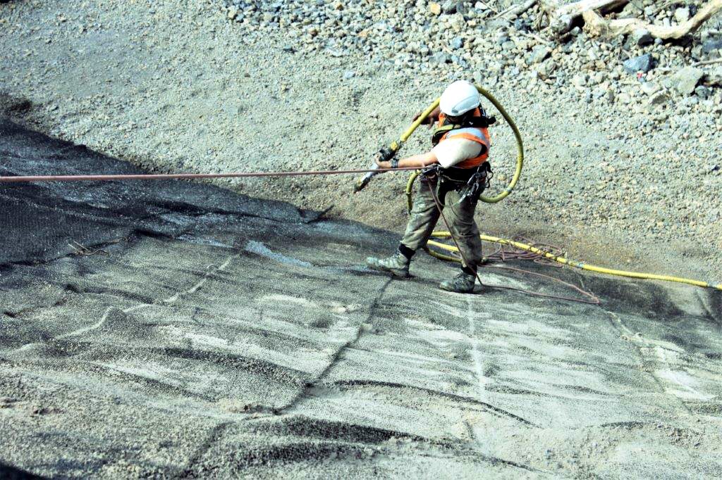 Roped-access operator hydroseeding a steep rock face
