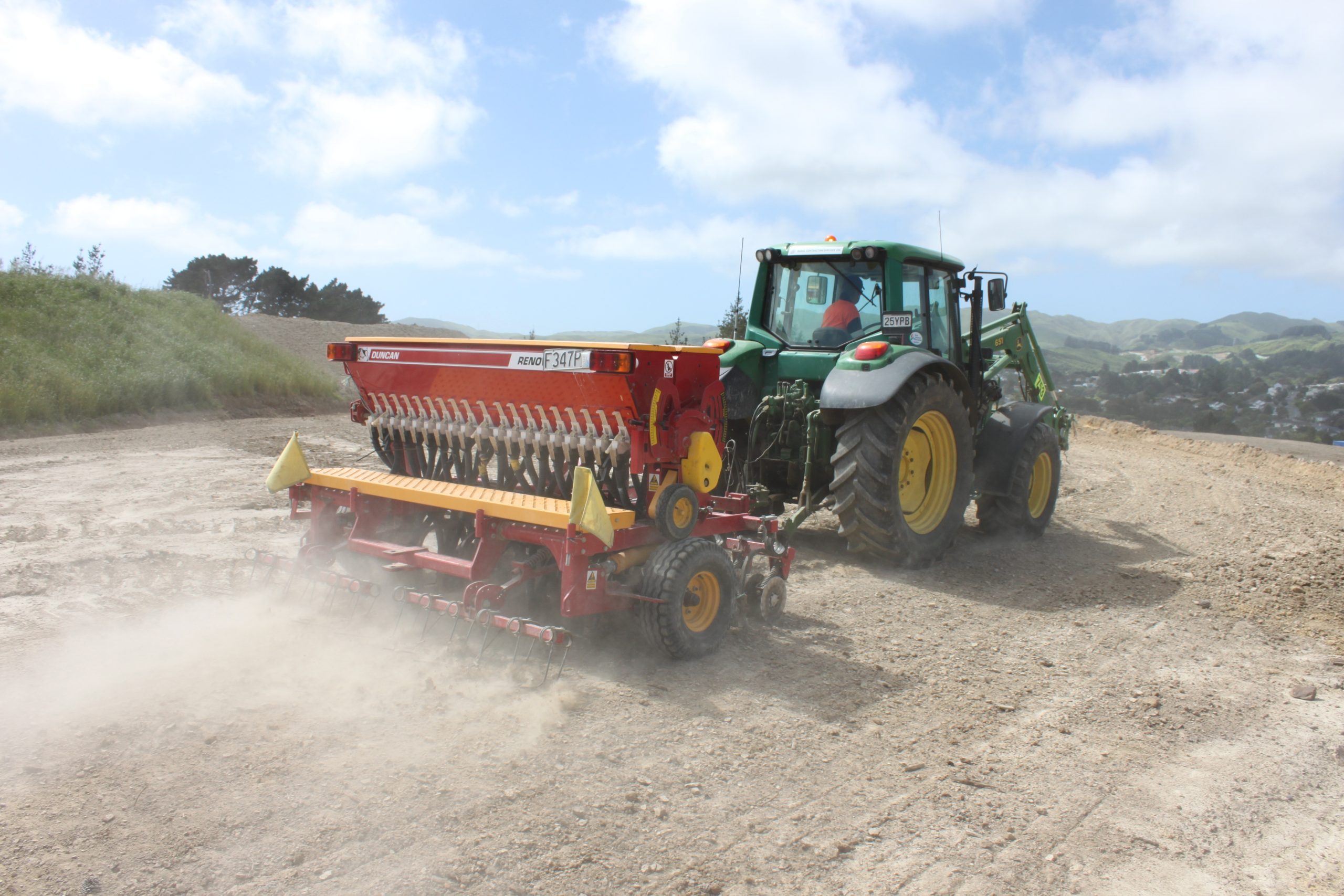 Tractor pulling a seed drill across a large prepared site