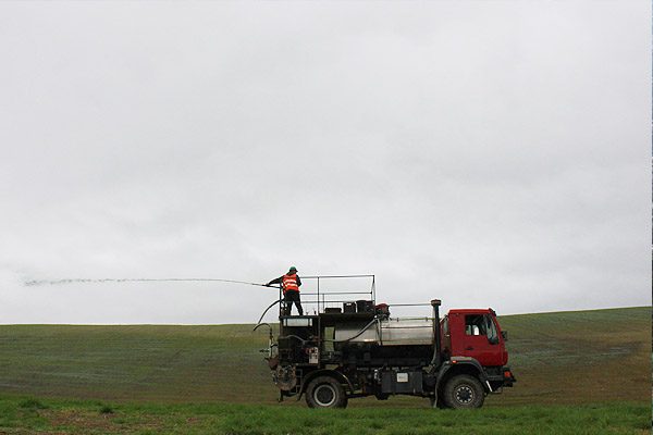 Operator spraying hydroseed from a truck-mounted cannon across open ground